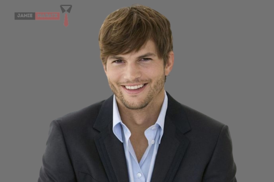 A smiling Ashton Kutcher in a black suit and light blue shirt, showcasing his professional and charismatic persona.