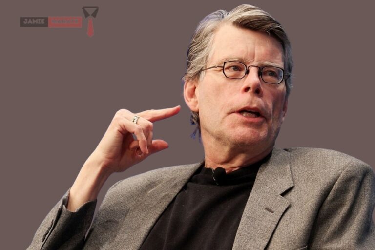 Stephen King speaking at an event, wearing a grey blazer, featured in the blog post "Stephen King Net Worth".