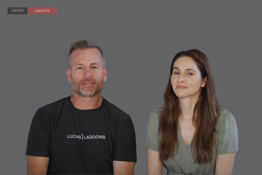 A man wearing a "Lucas Lagoons" t-shirt and a woman sitting beside him, both appearing in a video interview.