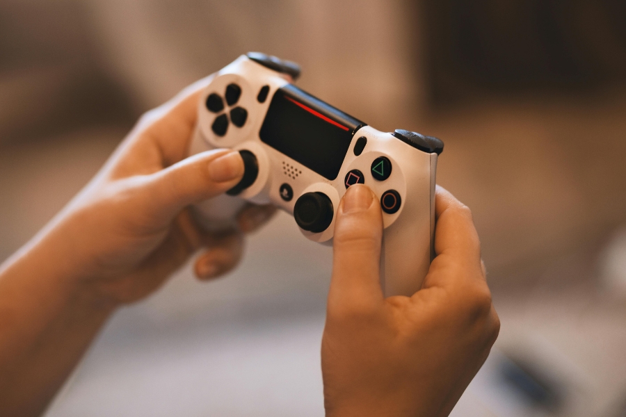 Hands holding a white gaming controller while playing a video game, representing the addictive gameplay experience of Infinite Craft.