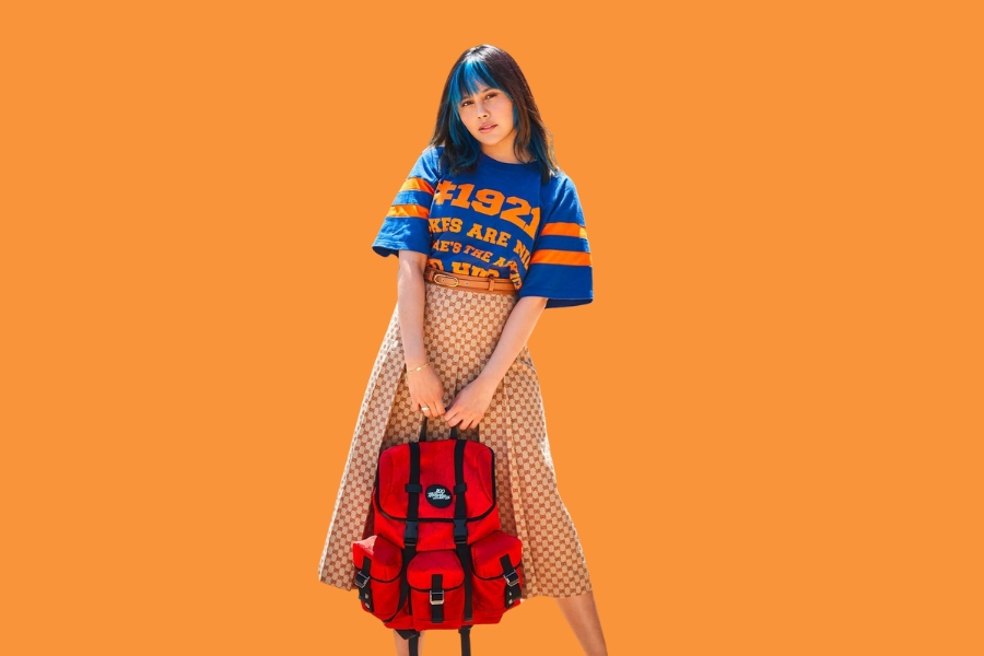 Neekolul wearing a graphic t-shirt and holding a red backpack, representing her role in the neekolul tax the rich controversy
