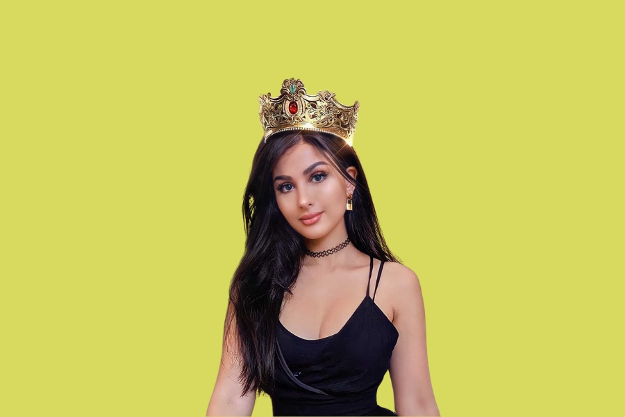 Sssniperwolf wearing a golden crown and black dress on a yellow background.