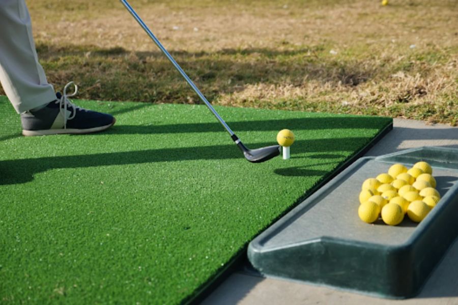 Golfer hitting from a synthetic golf mat with yellow practice balls at a home driving range setup