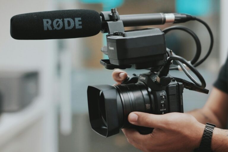 A person holding a professional Canon video camera with a mounted RØDE microphone, used for high-quality custom video content creation.