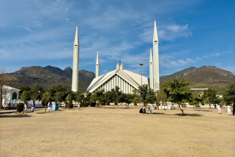 A wide-angle view of Faisal Mosque in Islamabad, Pakistan, with the scenic Margalla Hills in the background under a bright blue sky.